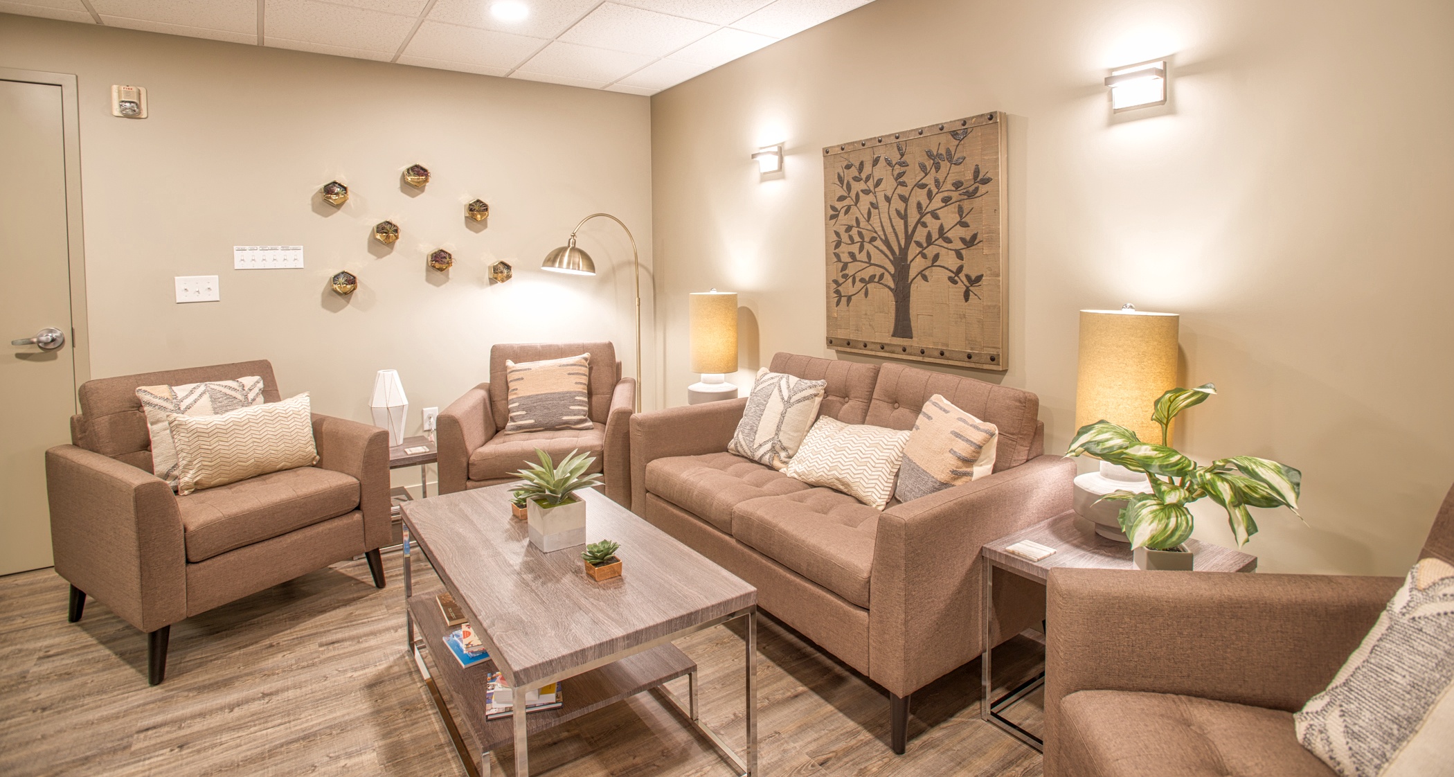 Waiting Room 4 A modern seating area with a beige furniture, throw pillows, light wood floors, framed artwork, and a coffee table.