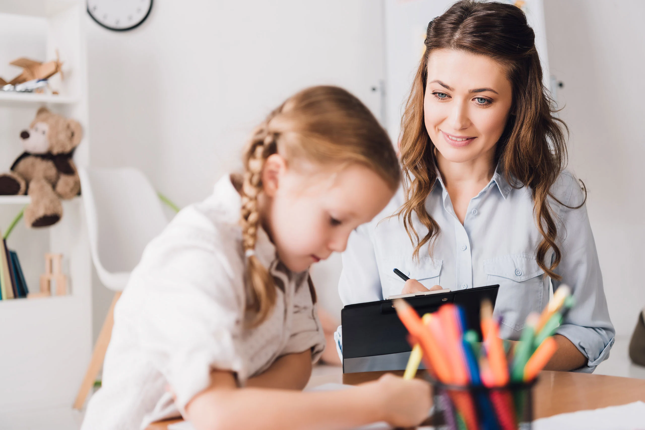 Assessments Children – Centered Connections A woman taking notes while observing a young child writing at a desk.