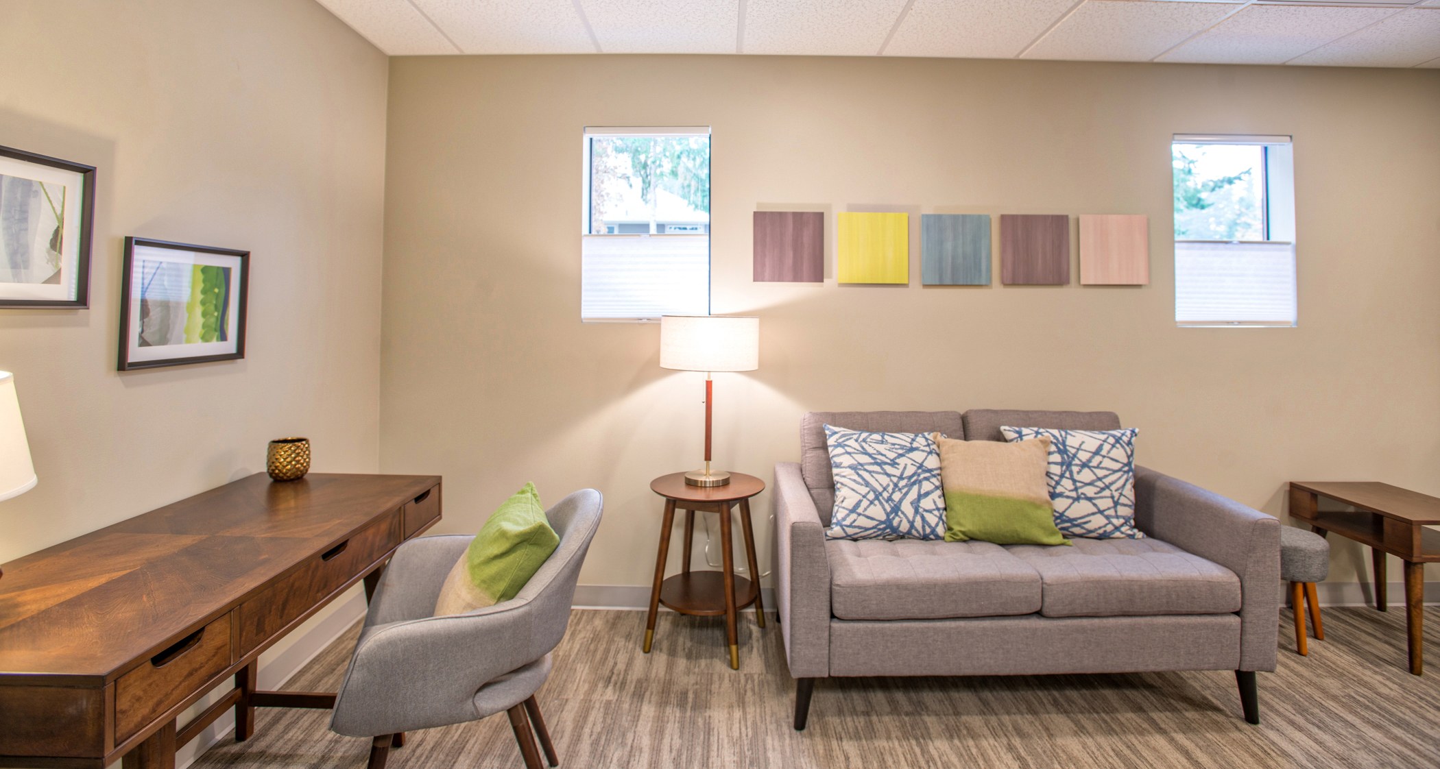 Couch A modern seating area with a gray loveseat, teal throw pillows, light wood floors, framed artwork, and a wooden desk.
