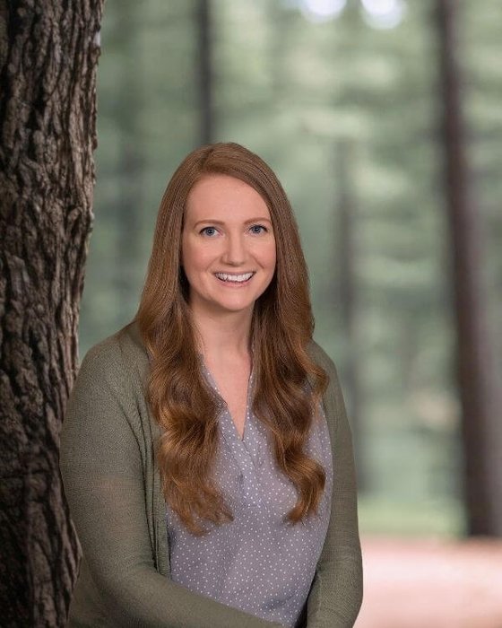 Lisa Criswell Outdoor portrait of a smiling woman with light brown hair in a softly focused wooded area.